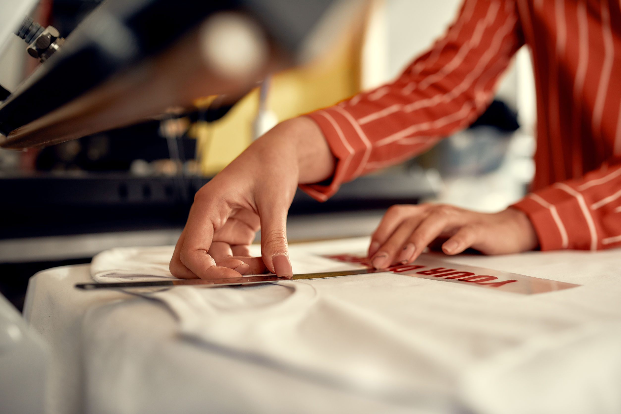 Cropped shot of woman hands trying on, moving advertisement sticker with text while preparing it to be printed on a T-Shirt. Printing on clothing and textiles concept. Horizontal shot