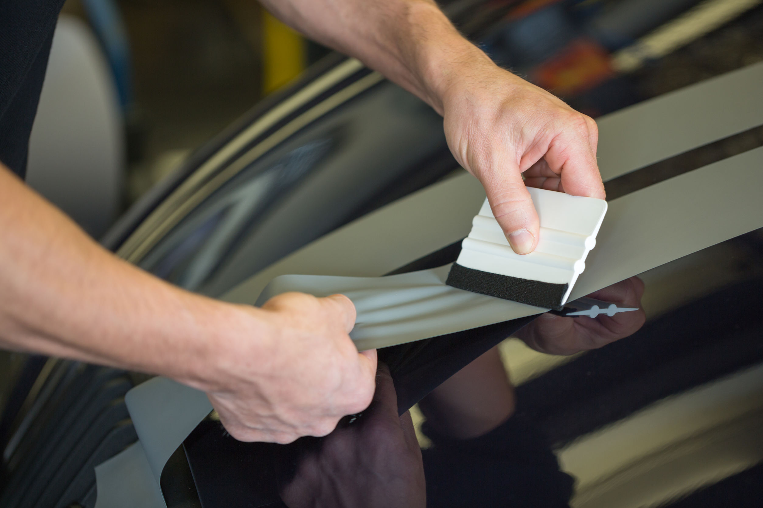 Car wrapper straightening wrapping foil with a squeegee to remove air bubbles